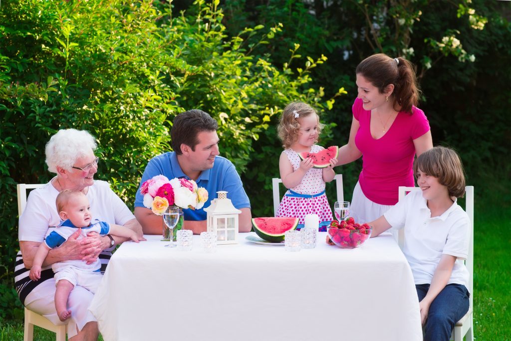 Big family with children have lunch outdoors. Parents with 3 kids and grandmother eat in the garden. Picnic for mother father baby boy toddler girl and teenager child. Generations and retirement.