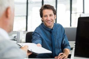 Close up of young businessman giving writing pad to senior businessman. Employees working in an office discussing about future. Businessman handling financial reports to leadership in office.