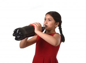 happy female child holding big cola soda bottle drinking isolated on white background in sugar drink abuse and addiction and sweet nutrition excess