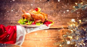 Christmas Holiday dinner. Santa Claus hand holding roasted Chicken. Christmas and New Year food concept, over rural wooden background and Decorated Christmas tree with lights.