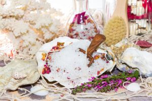 Marine bath salt mixed with aromatic rose petals displayed in a shell with bathing accesories and coral for a mineral rich rejuvenating bath
